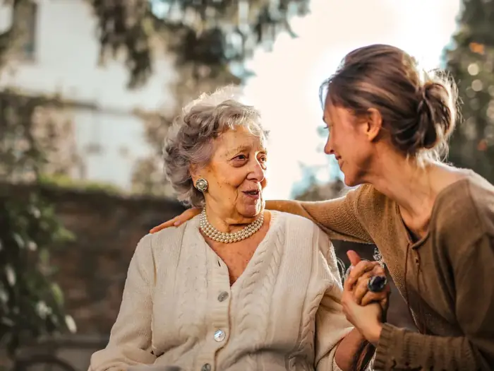 An older woman and her adult daughter talking and smiling outdoors in warm evening light